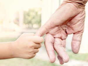 Hand of a child grasping to a single finger of an elderly adult.