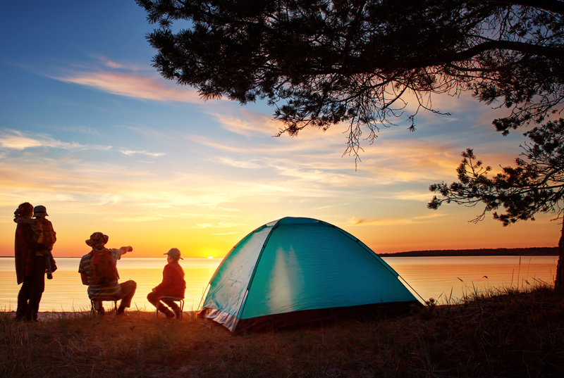 family of four camping by lake and viewing sunset